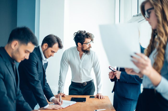 Successful team leader and business owner leading informal in-house business meeting. Businessman working on laptop in foreground. Business and entrepreneurship concept.