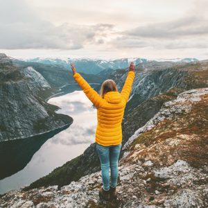 Happy woman raised hands on mountain summit traveling alone adventure lifestyle journey vacations aerial lake landscape success wellness emotions 