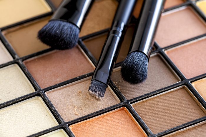 Three cosmetic brushes with light brown eye shadow dust sitting on top of palette of pale nude eye shadow shades