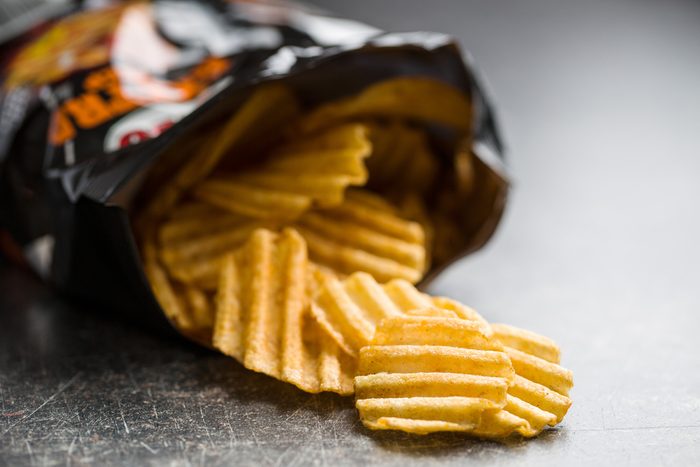 Crinkle cut potato chips on old kitchen table. Potato chips poured out from packing.