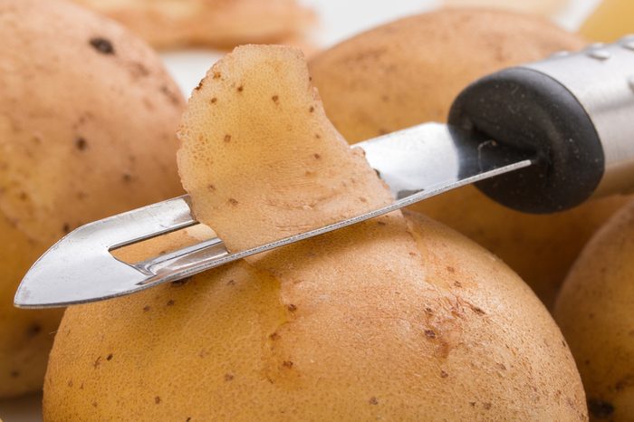 Potatoes, with a vegetable peeler on a white background, close up