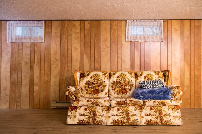 old couch from the 70s, in a basement, with a pillow and a blanket