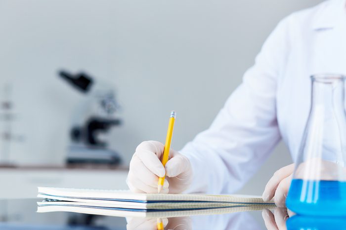 Hand of chemist with pencil writing down observations in laboratory
