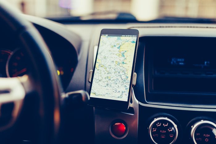 The map on the phone in the background of the dashboard. Black mobile phone with map gps navigation fixed in the mounting. Vintage style photo