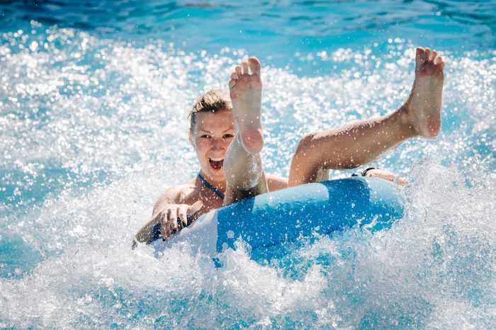 Funny girl taking a fast water ride on a float splashing water. Summer vacation with water park concept.