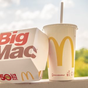 A Big Mac box and drink cup sit on a ledge, with a blurred green landscape and blue sky in the background.