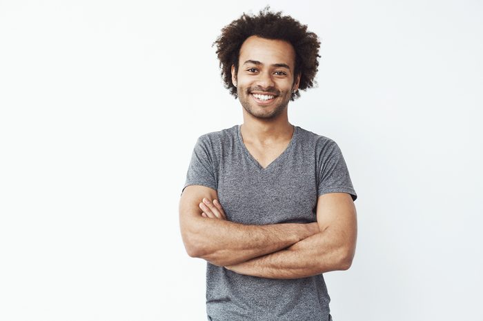 Portrait of stong and handsome african male student looking at camera smiling with crossed arms over white wall. Soon to be startup owner or salesman.