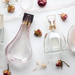 Perfume bottles arranged on a white surface surrounded by dried roses and delicate flowers, creating an elegant and romantic display.