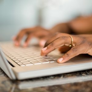 Hands typing on a laptop keyboard, resting on a marble surface in a well-lit room.