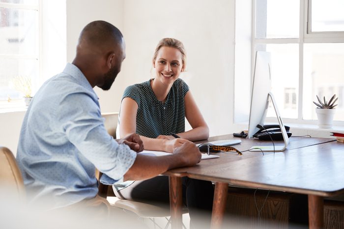 Man and woman sitting at a desk talking in an office smiling