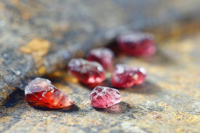 Uncut gemstones, red almandine garnets, from Lapland, displayed on a rusty gold pan