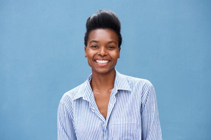Close up portrait of beautiful young black woman smiling against blue background