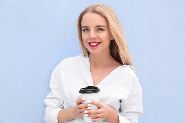 Beautiful young woman with cup of coffee near color wall