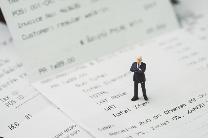 Tax, accounting and business expenses concept, miniature businessman figure standing on printed payment invoice or receipt around VAT line.