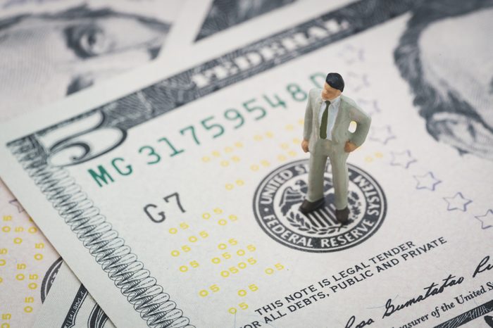 Miniature businessman leader standing and thinking on US Federal Reserve emblem on five dollars banknote as FED consider interest rate hike, economics and inflation control.