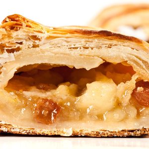 Pastry filled with apple and raisins, sliced to reveal layers, rests on a white background.