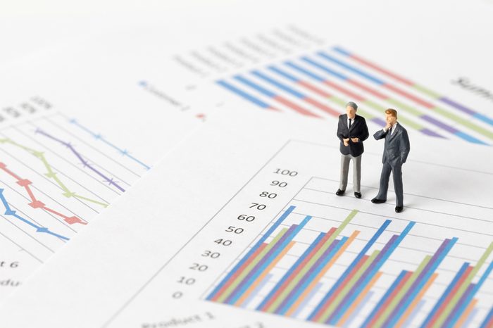 Miniature model of businessman thinking with project for presenting investment concept on graph.