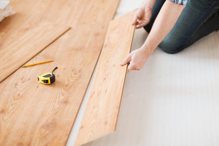 repair, building and home concept - close up of male hands intalling wood flooring