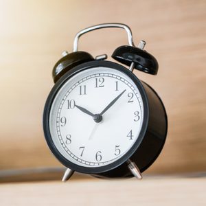Alarm clock displays time at 10:10, sitting on a wooden surface in a softly lit room.