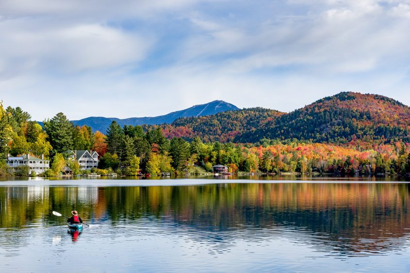 A panoramic view of Mirror Lake in Lake Placid, New York, on a sunny autumn day with colorful fall foliage on the mountains in the background