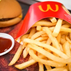 Fries spill from a red carton beside a hamburger and ketchup cup on a restaurant tray.