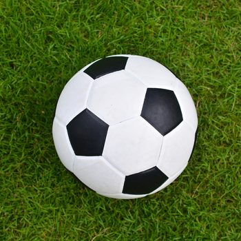 A soccer ball rests on vibrant green grass, contrasting its black and white pattern against the lush background.