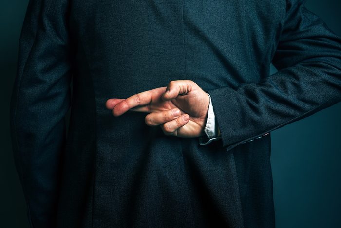 Dishonest businessman telling lies, lying male entrepreneur holding fingers crossed behind his back