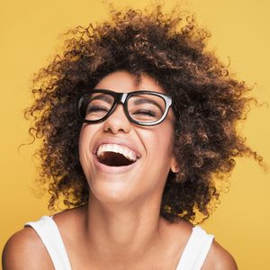 Person laughing energetically, wearing glasses, in front of a vibrant yellow background.