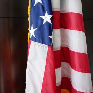 American flag hangs with stars and stripes visible, set against a plain, dark background.