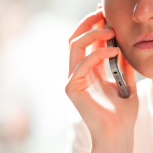 A person holds a smartphone to their ear, speaking, with a softly blurred background.