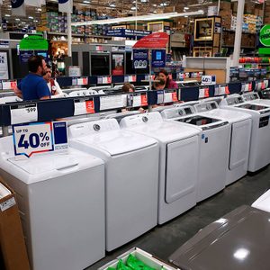 Washing machines displayed, offering up to 40% off, in a brightly lit appliance store with customers browsing nearby.