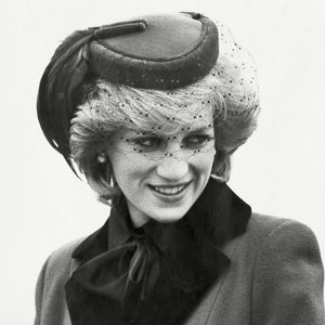 Woman smiling, wearing hat with veil and coat, in a black-and-white portrait.