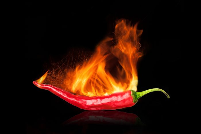single red chili peppers with fire on black background