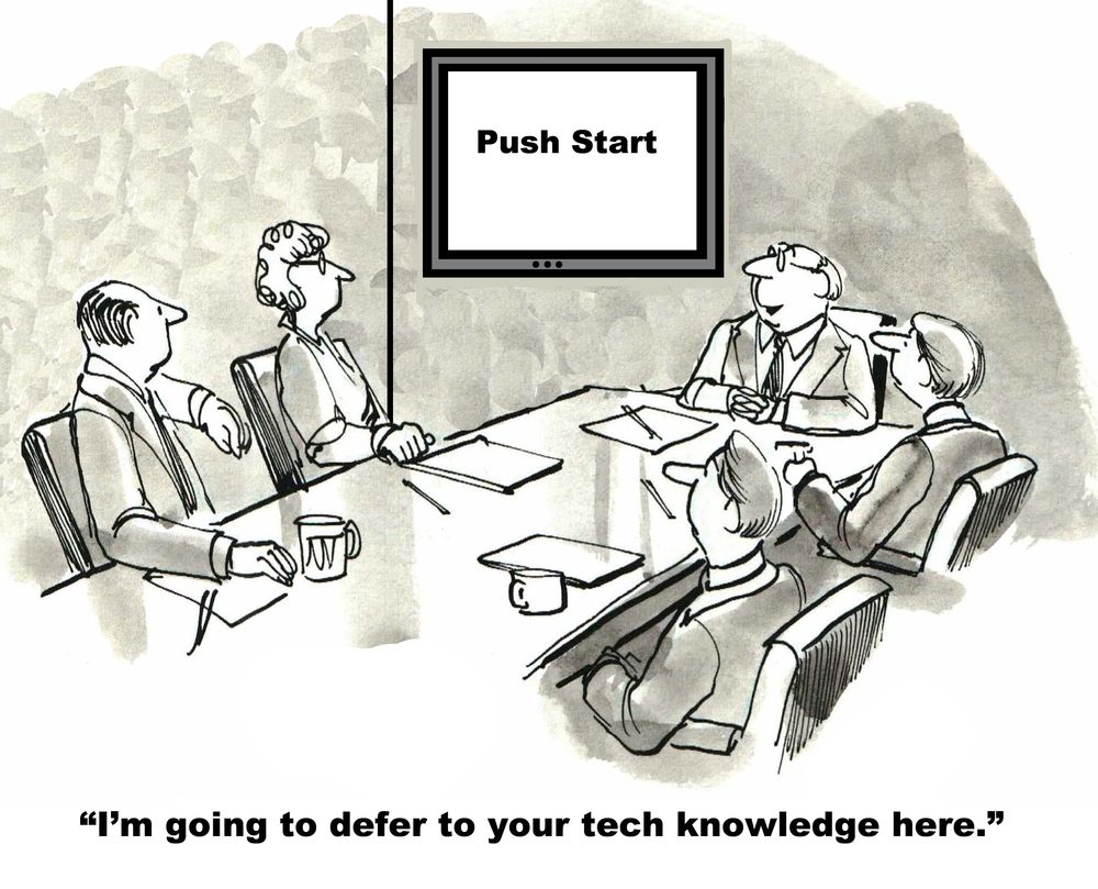 Businesspeople sit around a conference table, staring at a screen with "Push Start." Caption: "Iâ€™m going to defer to your tech knowledge here."