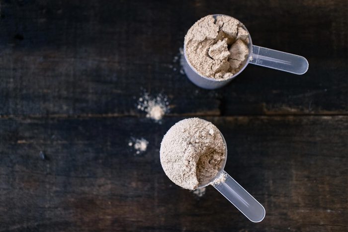 Whey powder in measuring scoops on wooden background.