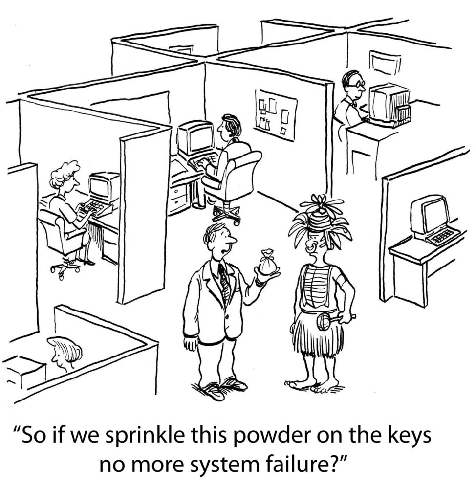 Man holds a bag of powder, speaking to a woman in tribal attire; office workers sit at computers in surrounding cubicles. Text: "So if we sprinkle this powder on the keys no more system failure?"