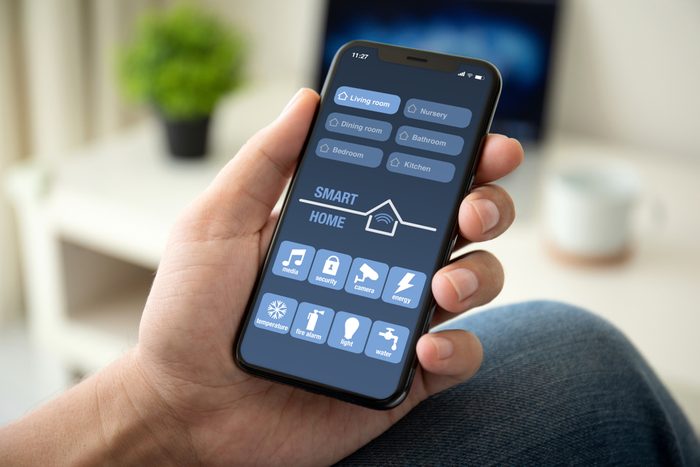 man hand holding phone with app smart home in room house