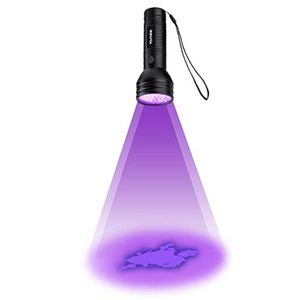 Flashlight emits purple light revealing stains on white background, with a hand strap attached.