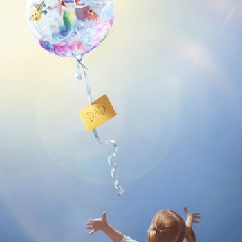 Balloon with a mermaid floats upwards, tethered by a ribbon with a card labeled "DAD." A child with outstretched arms reaches towards it.
