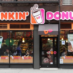 Dunkin' Donuts storefront displays coffee posters; people sit inside visible through the glass.
