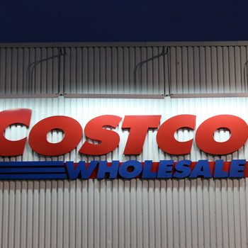 Sign displays "COSTCO WHOLESALE" in bold red and blue letters, mounted on a corrugated metal wall.