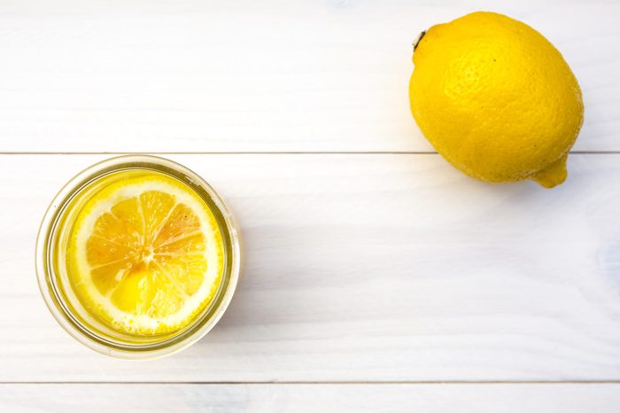 Yellow juice dessert with a lemon on brown wooden background, toned with soft pastel colors.