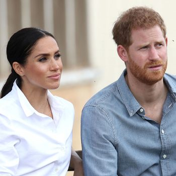 A seated man and woman look attentively into the distance; he wears a denim shirt, she wears a white blouse, outdoors.