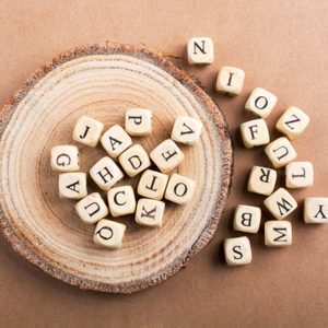 Wooden letter cubes rest on a tree slice against a brown background, forming a scattered pattern.