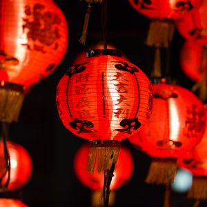 Red lanterns hang glowing, adorned with black patterns and Chinese characters, against a dark background.