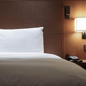 White pillows rest on a bed; glowing lamp on wooden wall, clock displaying 08:54, and telephone placed on bedside table.