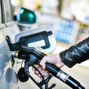 A hand holds a fuel nozzle, refueling a car at a gas station.