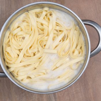 Pot with boiling pasta, releasing steam on a wooden surface.