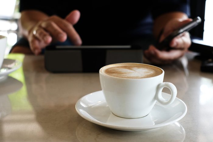 Hot latte coffee in white cup and man use tablet in cafe.