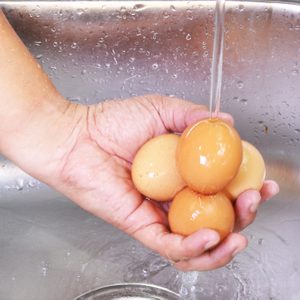 Hand rinsing four eggs under running water in a stainless steel sink.